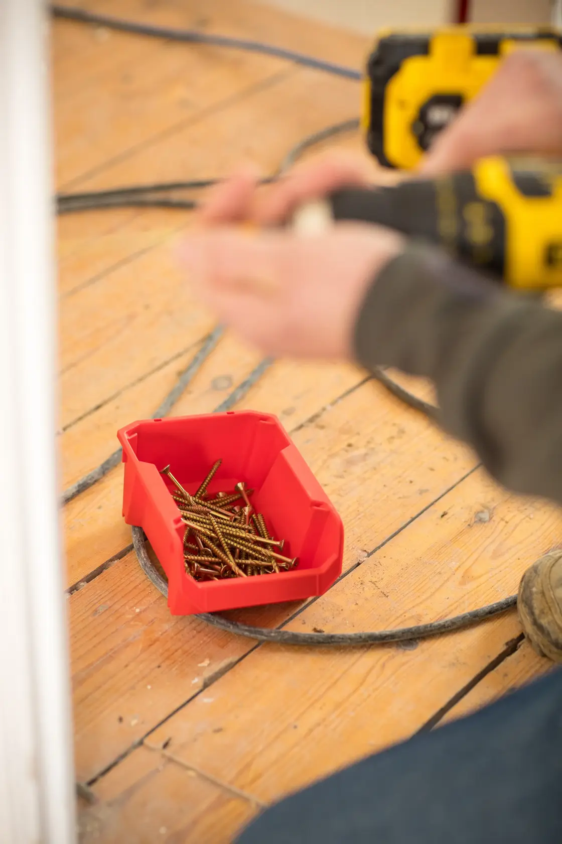 STANLEY STST82736-1 red storage bin holding screws on wooden floor, angled view, tradesperson working nearby.