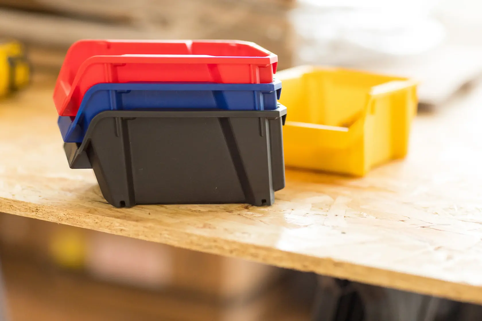 STANLEY STST82736-1 stackable plastic storage bins in red, blue, black and yellow on a wooden surface.