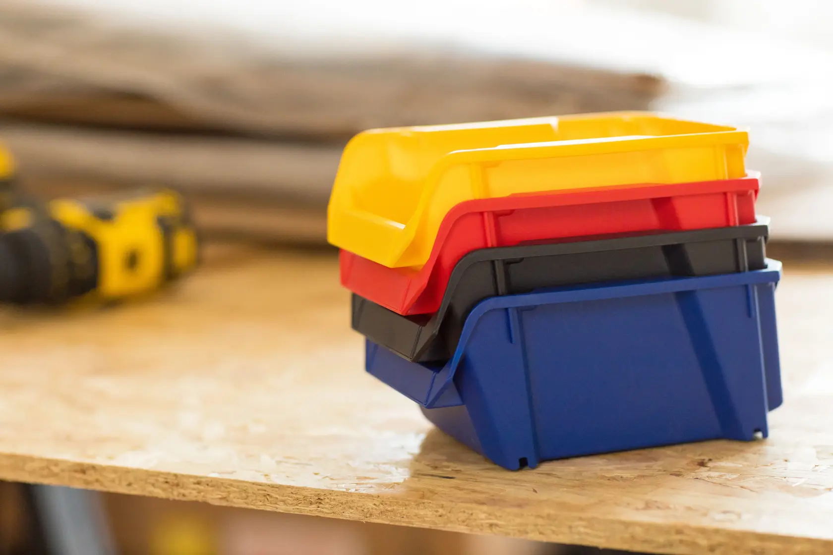 STANLEY STST82740-1 stackable plastic storage bins in yellow, red, black, blue on a workbench, side angle.