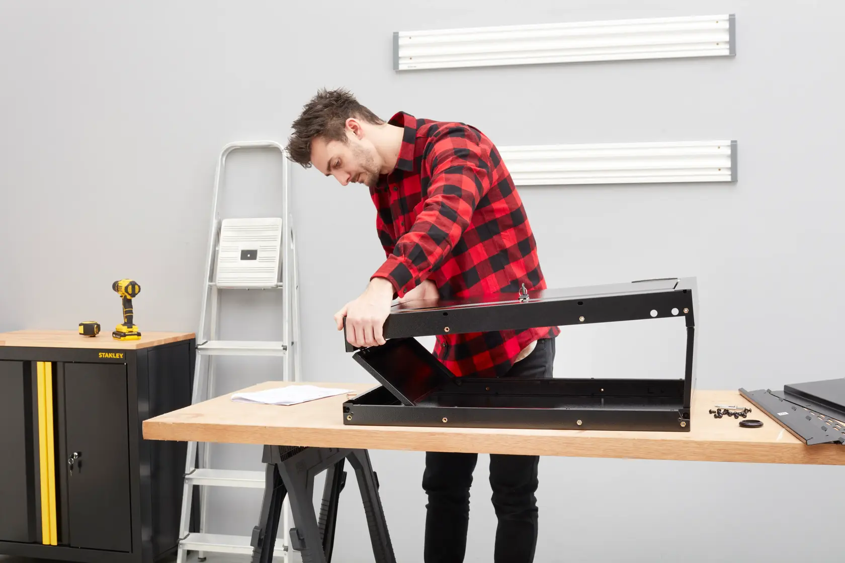 STANLEY STST97599-1 photography of person assembling black metal cabinet on a wooden workbench.